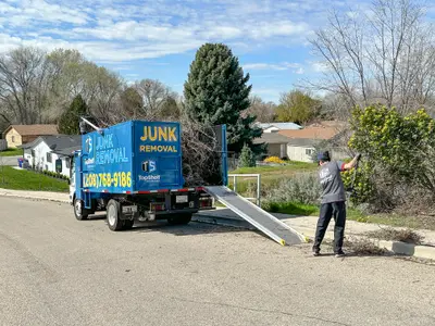 Top Shelf Junk Removal crew member loading branches with truck ramp in Meridian Idaho